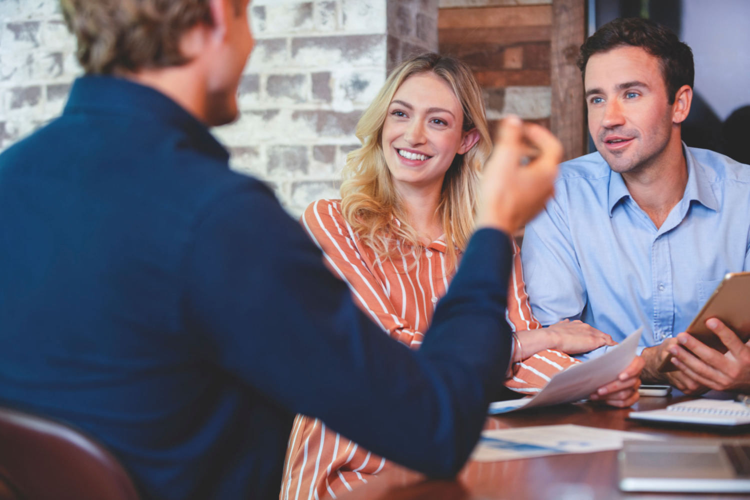 Young couple meeting with an advisor or business person. They are holding documents and talking. Could be discussing banking, finance, insurance etc. They are happy and smiling